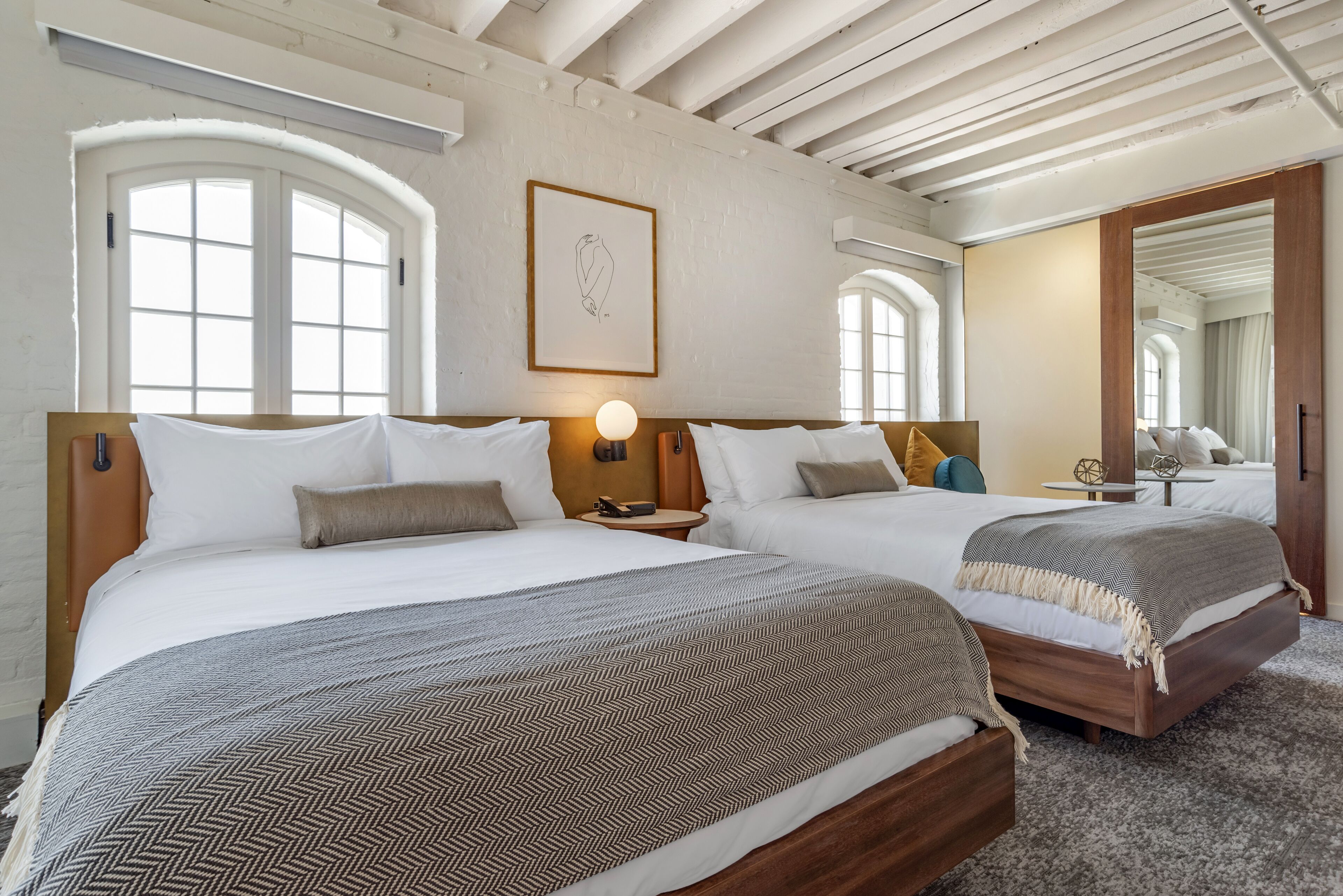 Habitación de hotel con dos camas, un ventanal grande, una obra de arte enmarcada y techo de madera.