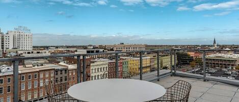 A rooftop terrace with a round table and four chairs, offering a panoramic view of a cityscape with historic buildings and a church spire.