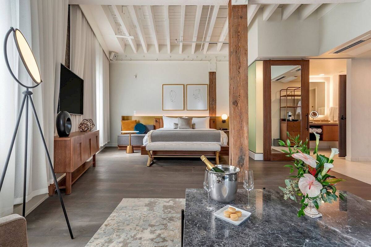 A modern hotel room with a bed, bedside table, and a view of the hallway.