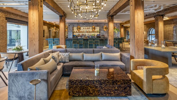 A modern lounge area with a sectional sofa, a coffee table, and a bar in the background. - ONE11 Hotel (New Orleans)