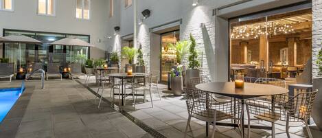 Un patio al aire libre con piscina, mobiliario y vistas a un restaurante.