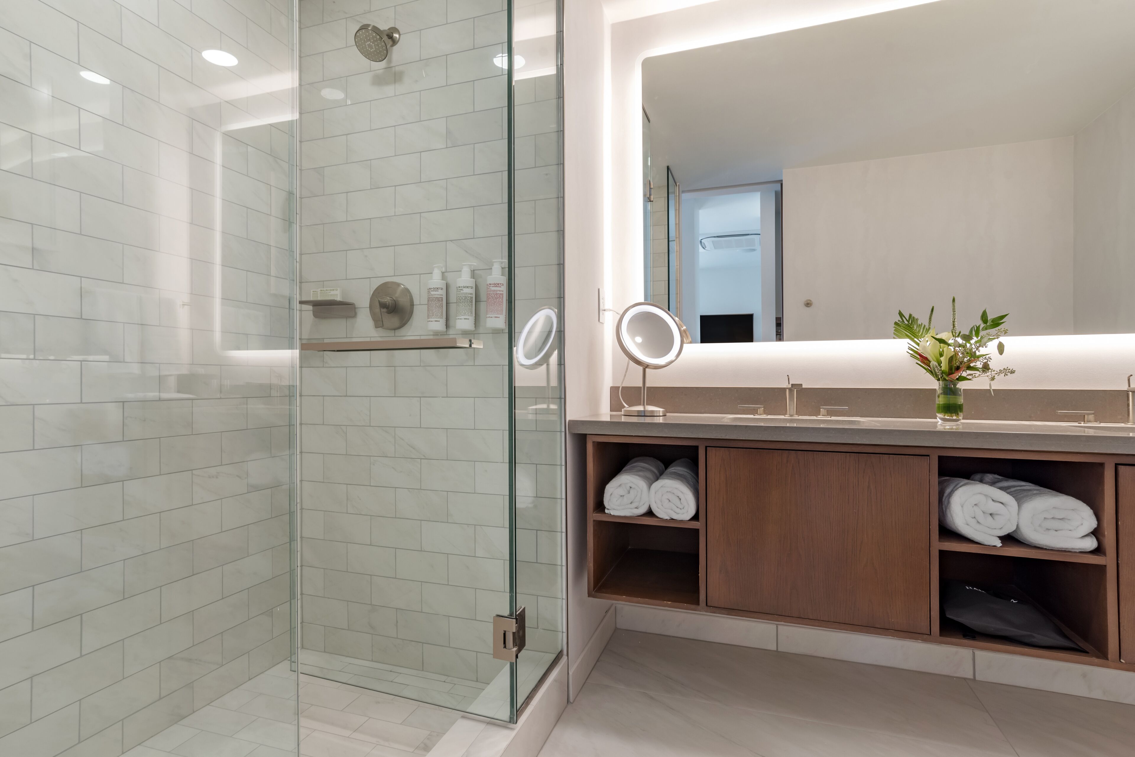 A modern bathroom with a glass shower enclosure, a vanity with a mirror, and neatly folded towels.