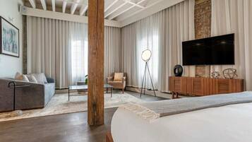 A modern bedroom with a large bed, a TV, a wooden cabinet, and a seating area with a chair and a small table.