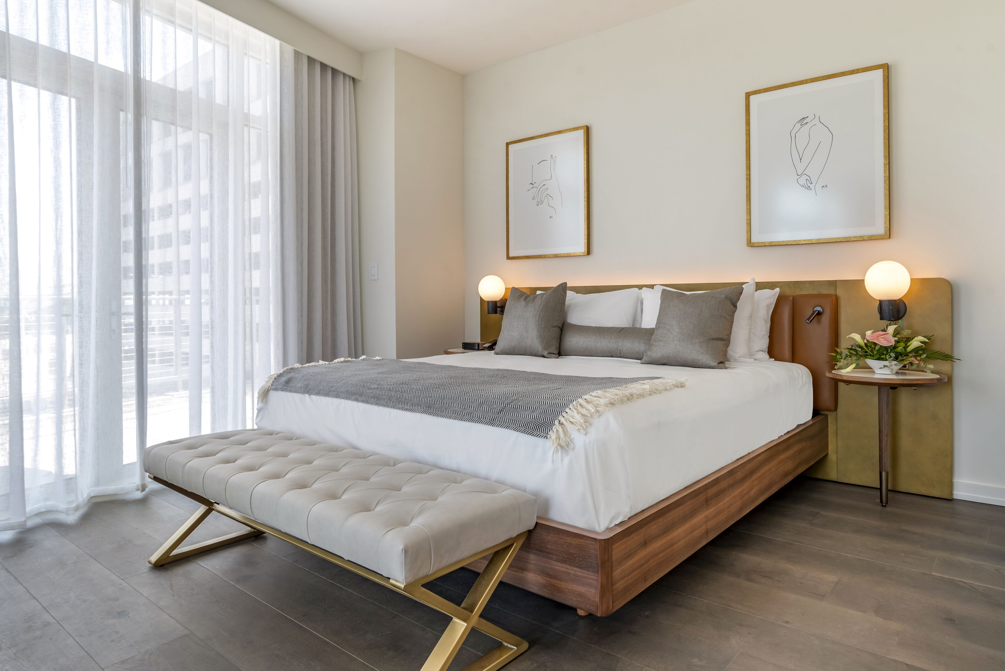 Ein modernes Schlafzimmer mit einem großen Bett, einer Bank und zwei gerahmten Kunstwerken an der Wand.