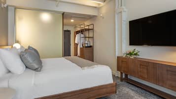 A modern bedroom with a wooden bed frame, a flat-screen TV, and a wooden console table with a vase of flowers.