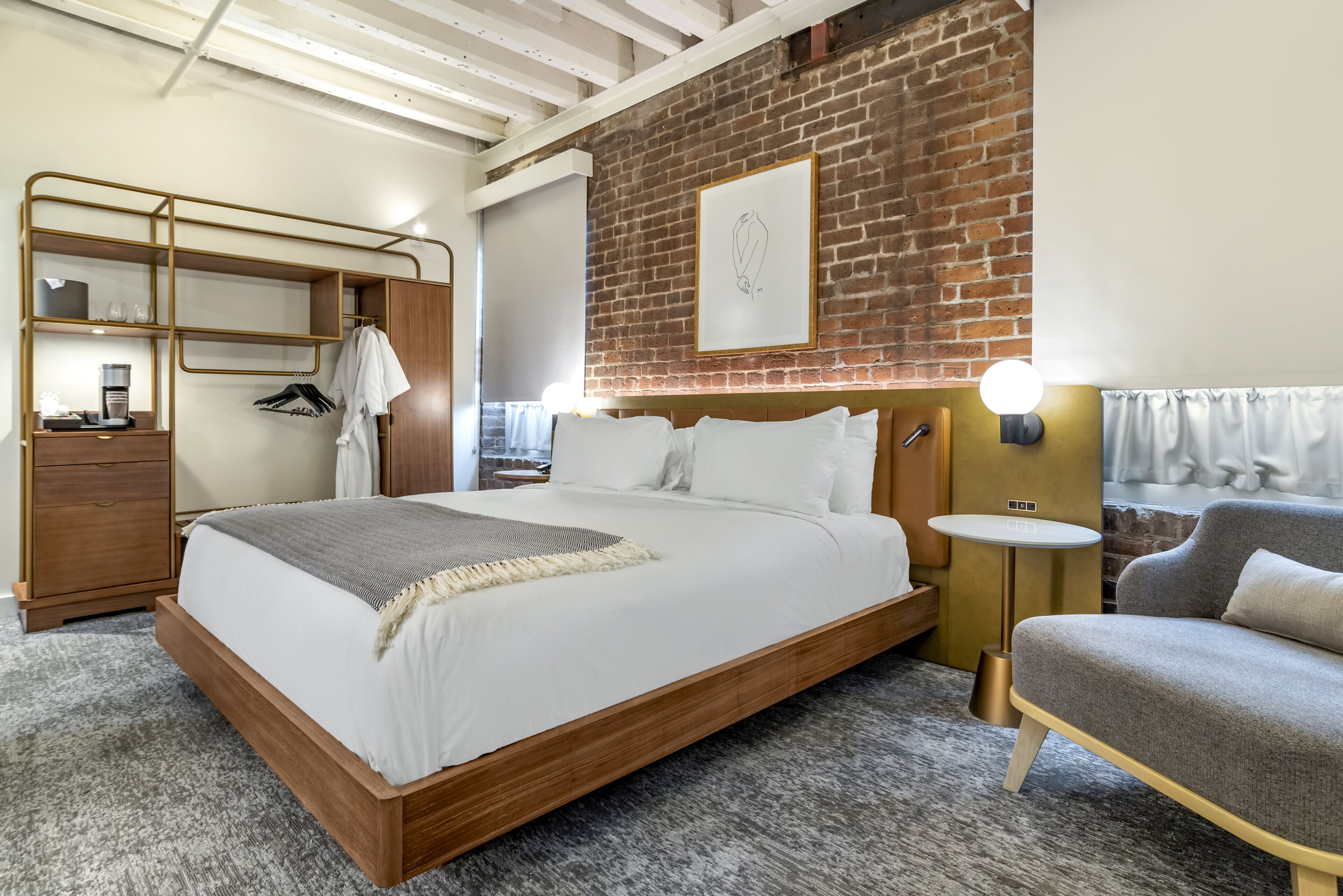 A modern hotel room with a wooden bed, a grey sofa, a small round table, and a brick wall.