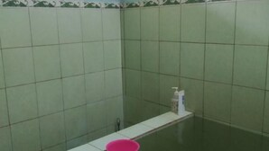 A bathroom with green tiles, a window, and a pink bucket on the counter. - Homestay Banyumili (Kalirejo)