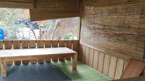A covered outdoor seating area with a wooden bench and a table. - Homestay Banyumili (Kalirejo)