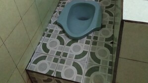 A small bathroom with a toilet, a broom, and a soap dispenser on the counter. - Homestay Banyumili (Kalirejo)