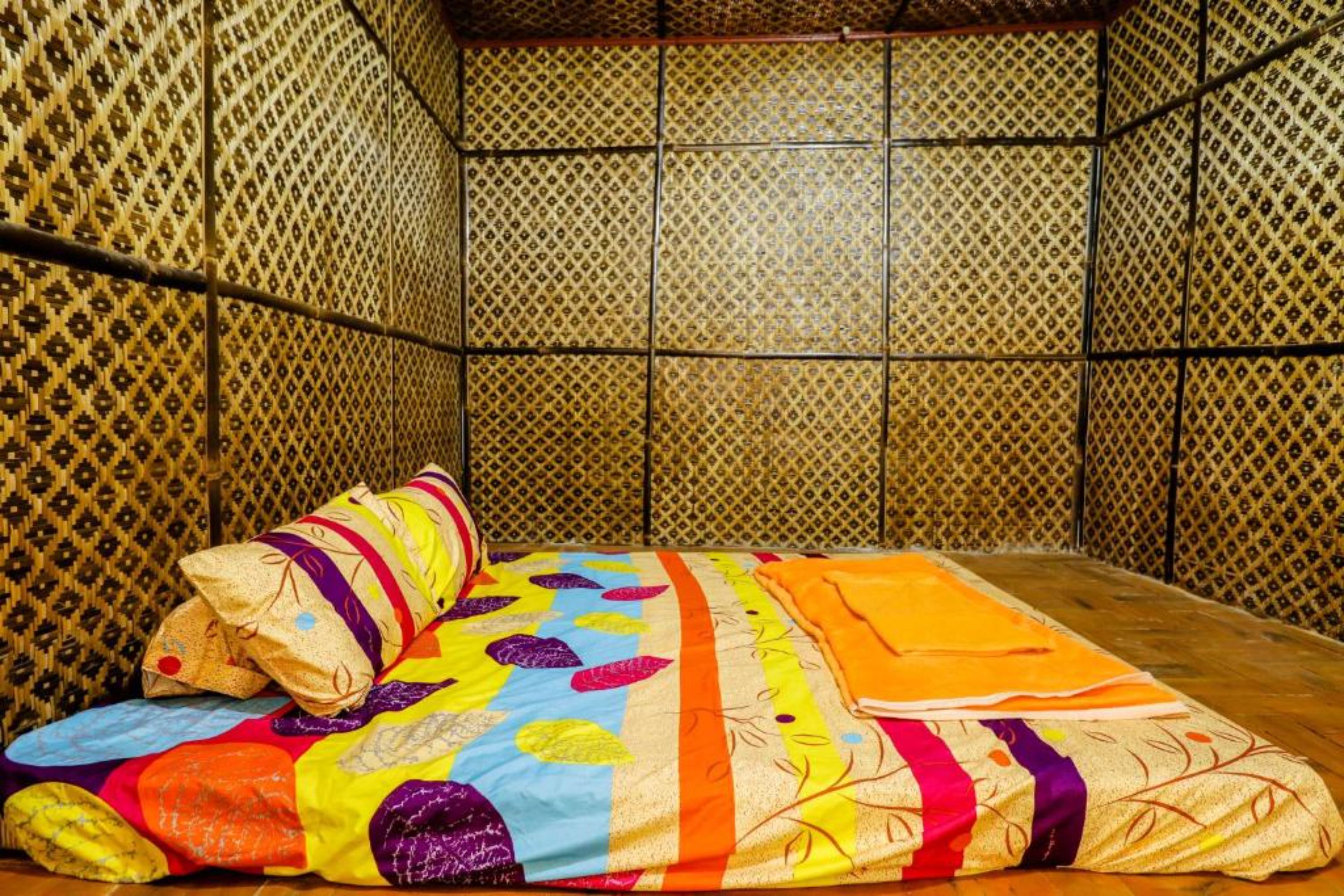 A room with a patterned wall, a bed with a colorful quilt, and a neatly folded blanket on the floor.