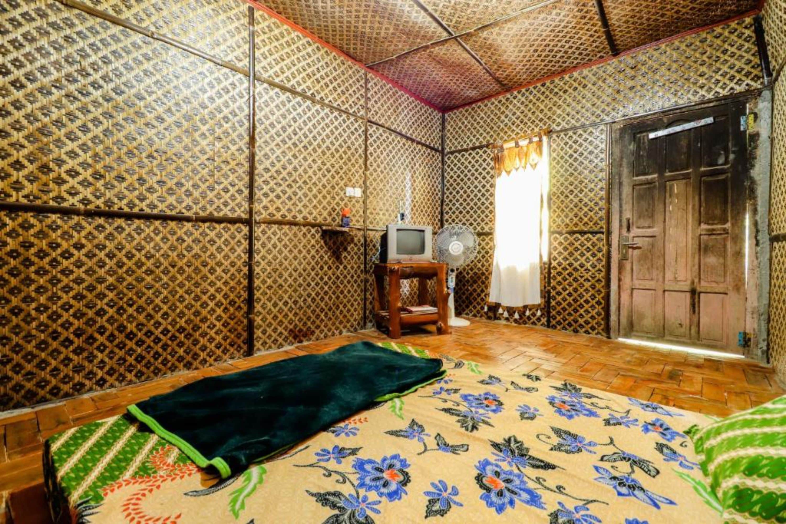 A room with patterned walls, a bed with a floral bedspread, a television, and a wooden door.