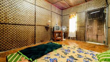 A room with patterned walls, a bed with a floral bedspread, a television, and a wooden door.