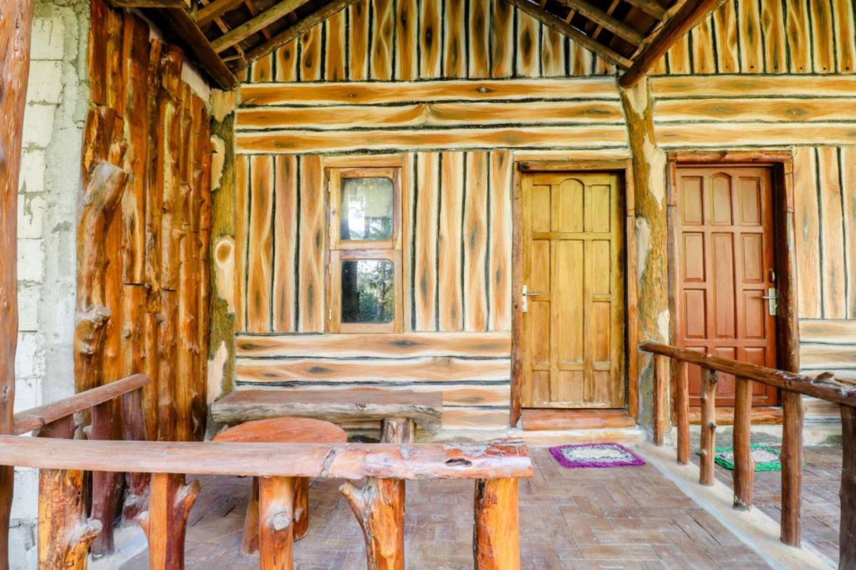 A rustic log cabin with a wooden bench, a small table, and a door with a window.