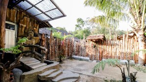 A rustic wooden house with a thatched roof, a bamboo fence, and a stone staircase leading to the entrance. - Larasati Homestay (Kalirejo)