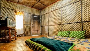 A room with a patterned wall, a bed with a floral bedspread, a wooden floor, and a television on a wooden table. - Larasati Homestay (Kalirejo)