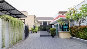 A paved courtyard with a black gate, potted plants, and a building with a red roof. - Khatarina Female Residence - Female Only - khusus wanita (Depok)