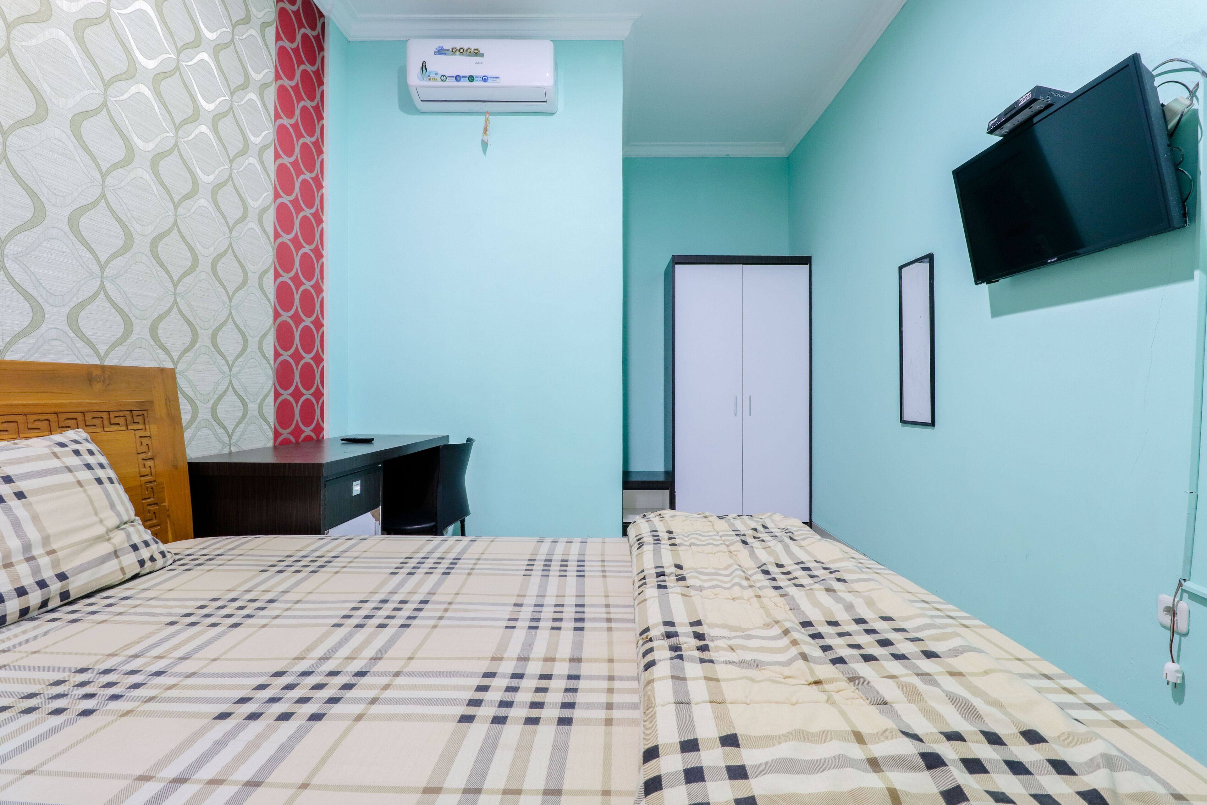 A room with two beds, a desk, a TV, and an air conditioning unit.