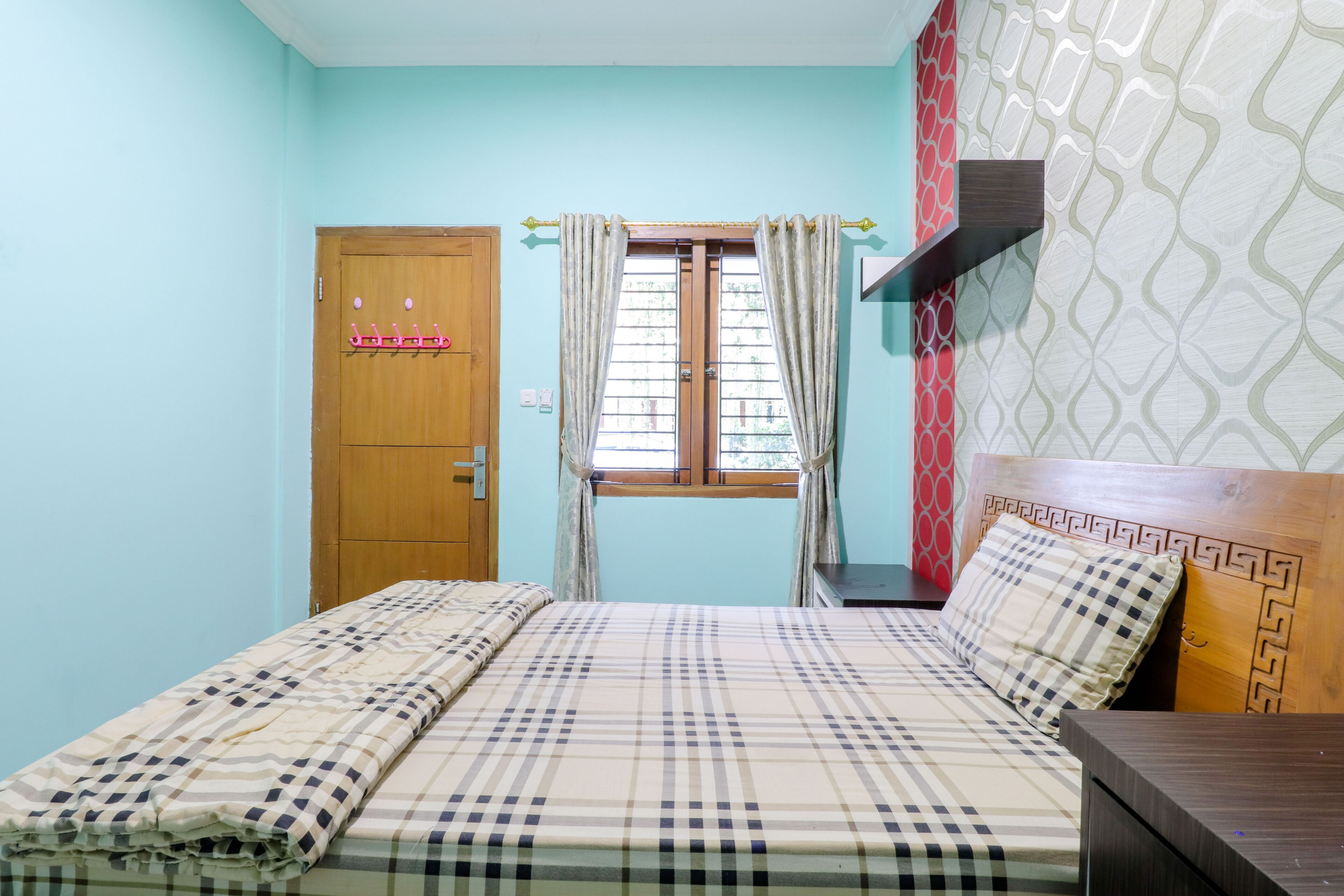 Un dormitorio con cama, una puerta de madera, una ventana con cortinas y un papel tapiz estampado.