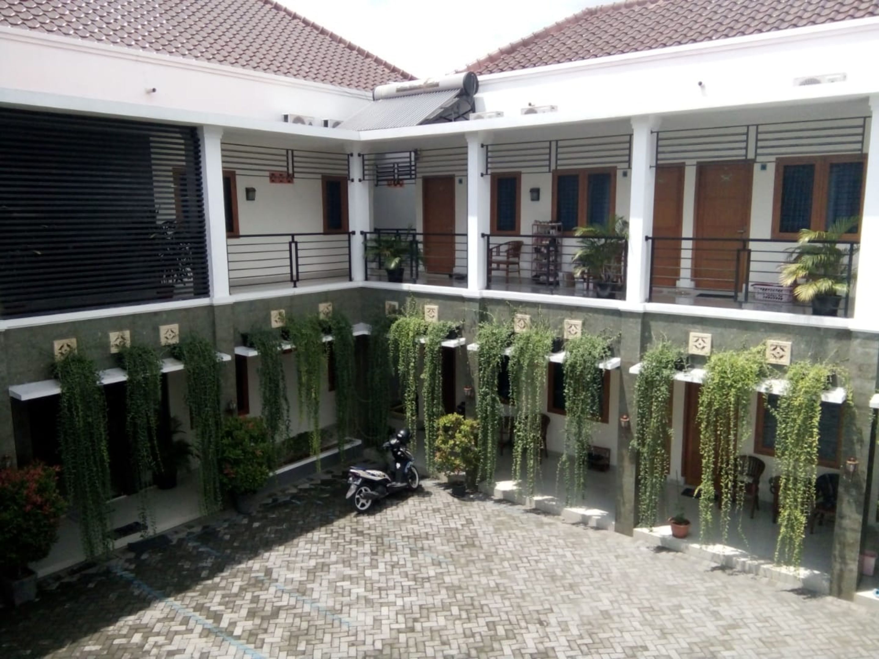 Un patio con suelo de baldosas, plantas en macetas y una scooter estacionada.