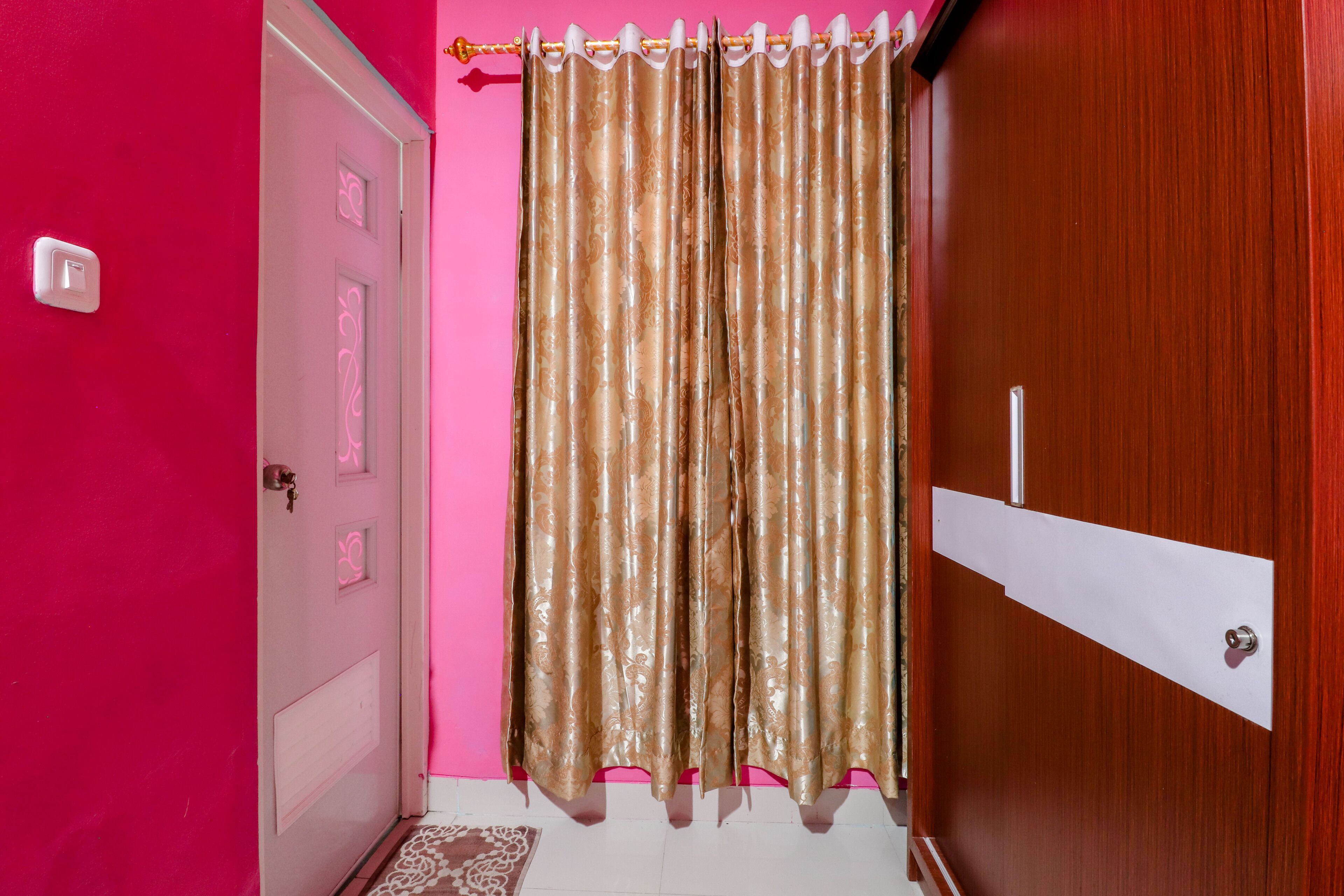 Ein Zimmer mit einer rosafarbenen Wand, einer Holztür und einem Vorhang.