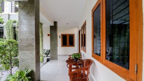 A corridor with a wooden table and chairs, potted plants, and large windows with wooden frames. - Khatarina Female Residence - Female Only - khusus wanita (Depok)
