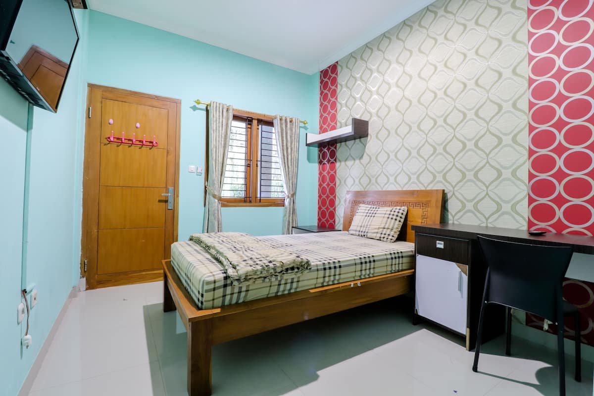 A bedroom with a bed, a desk, a chair, a wardrobe, and a window with curtains.