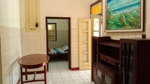 Quarto com mesa de madeira, cama com roupa de cama listrada, quadro na parede e um suporte para TV.