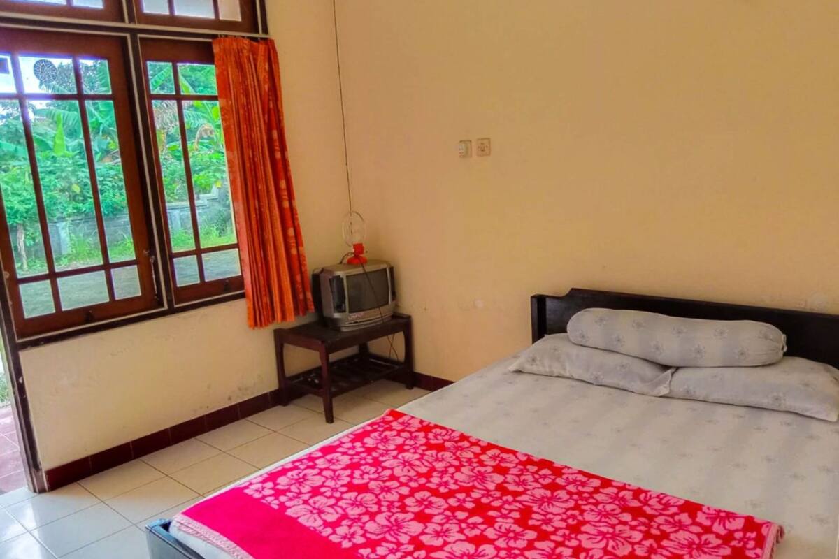A bedroom with a bed, a TV on a small table, and a window with curtains.