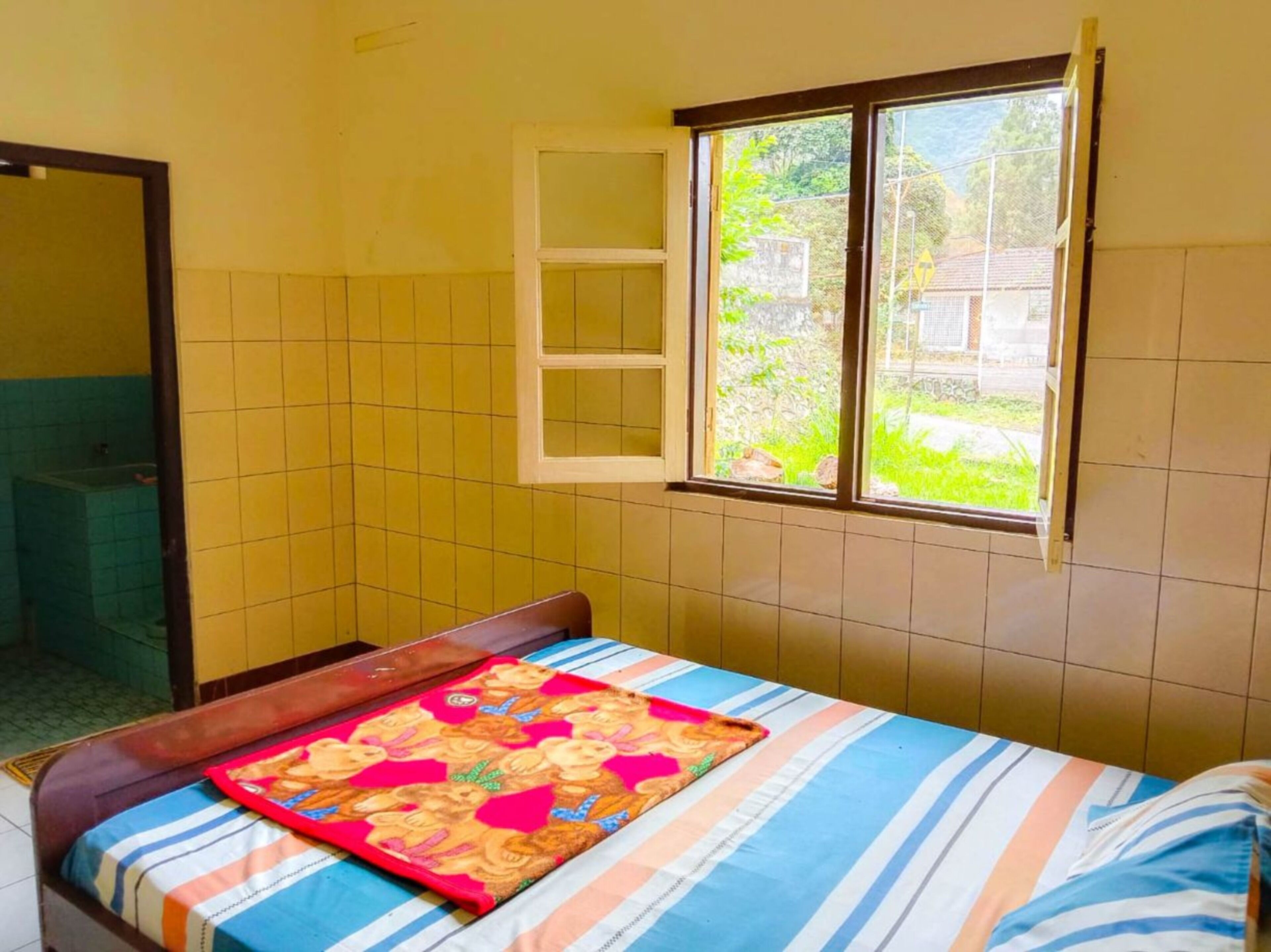 Una habitación pequeña con cama individual, ventana, espejo y un baño a la vista.