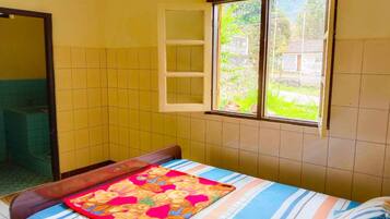 Una habitación pequeña con cama individual, ventana, espejo y un baño a la vista.