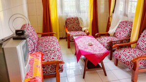 Quarto com sofá, duas poltronas, uma mesinha e televisão.
