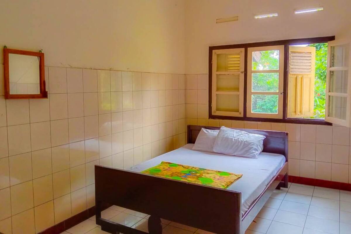 A bedroom with a bed, a window with shutters, and a tiled wall.