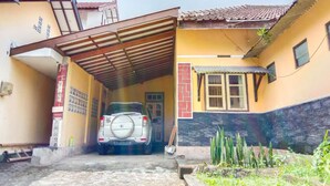 Um carro estacionado em área coberta de garagem, com uma casa ao fundo.
