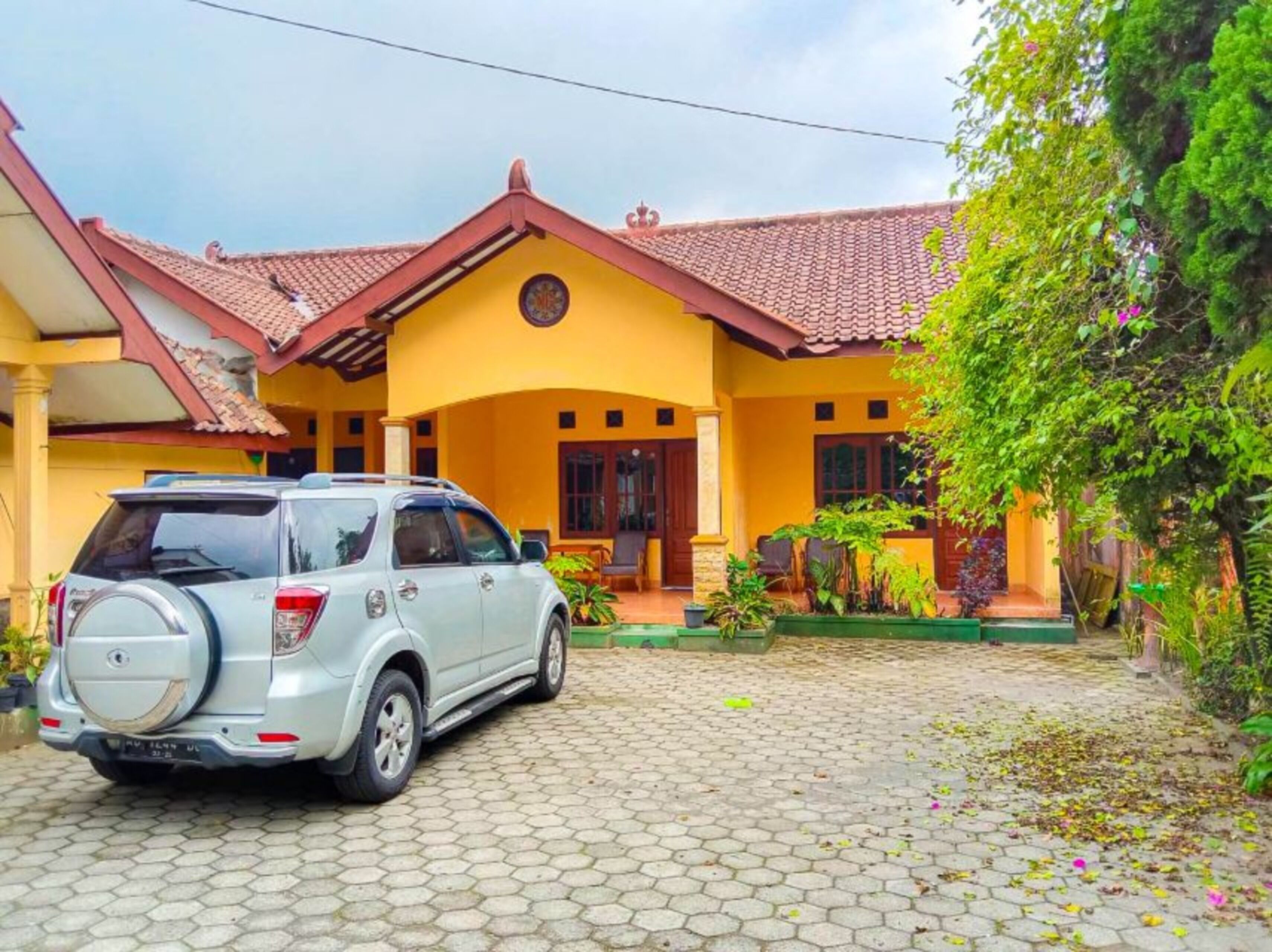 A house with a tiled roof, a parked SUV, and a garden with various plants.
