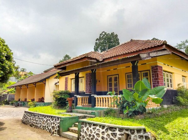 A two-story house with a tiled roof, yellow walls, and a porch with a balustrade. - Nguntara Gati (Pakem)