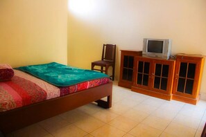 A bedroom with a bed, a television on a wooden cabinet, and a chair. - Nguntara Gati (Pakem)