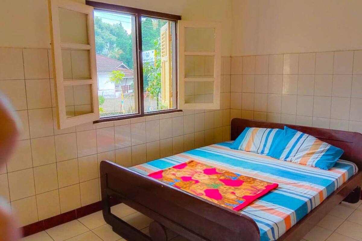 A bedroom with a bed, a window, and a view of greenery outside.