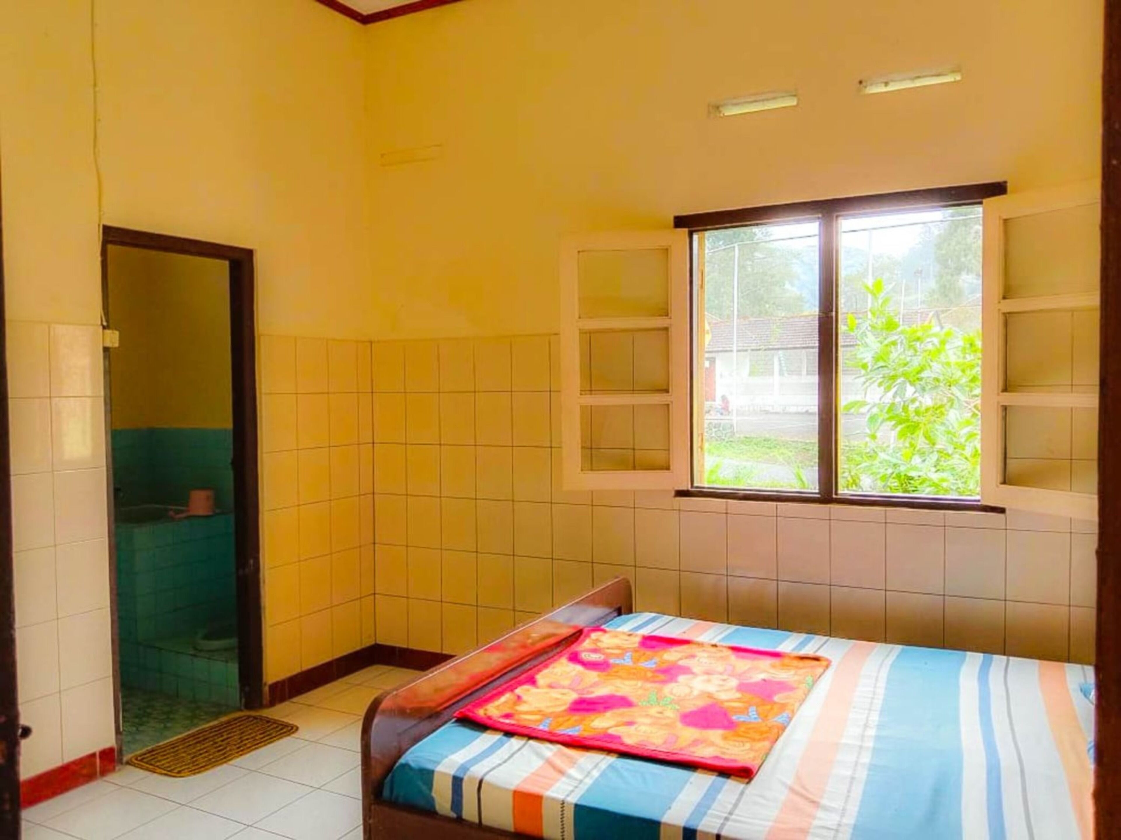 A small, clean room with a bed, a window, and a bathroom visible through an open door.