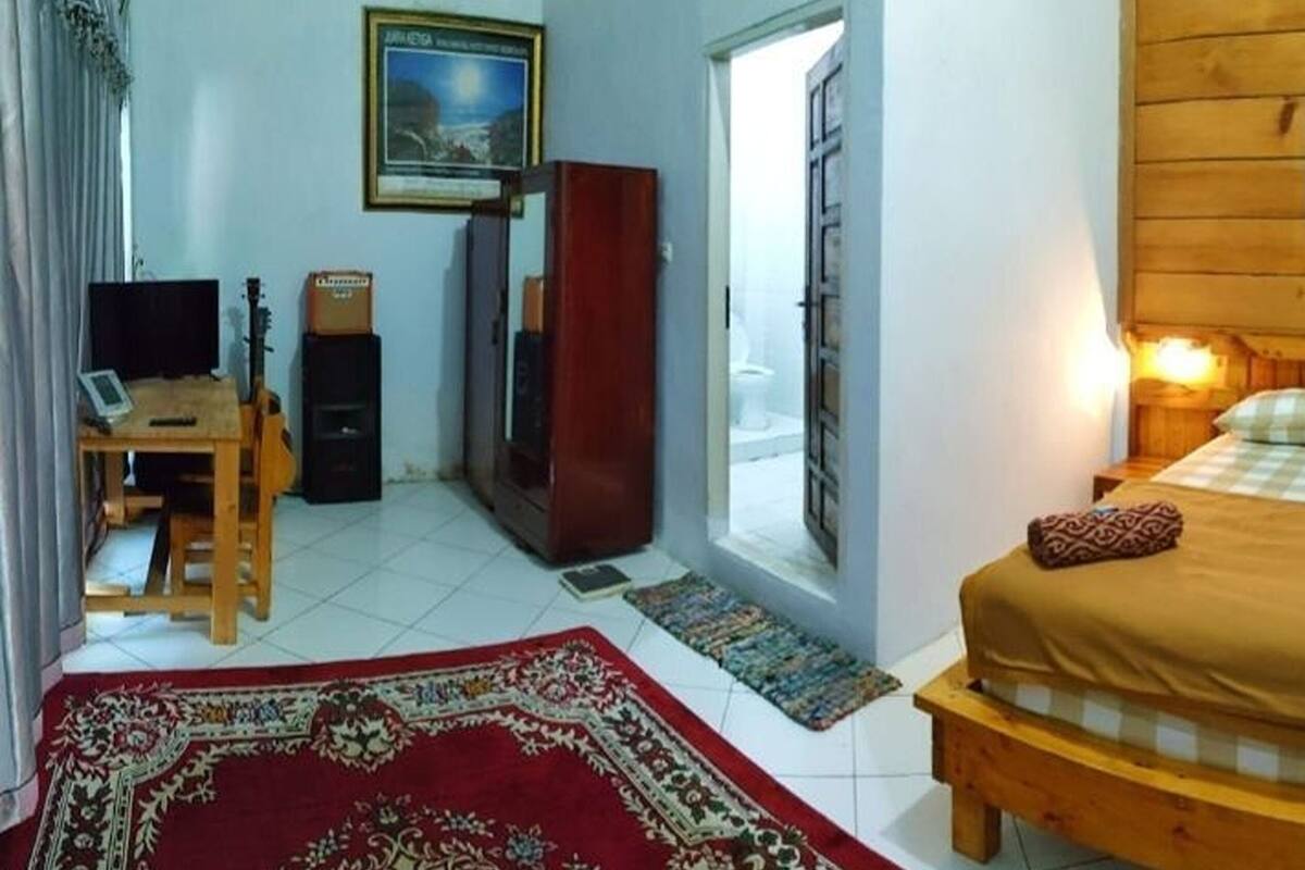 Una habitación con cama, escritorio con computadora, una guitarra y armario.