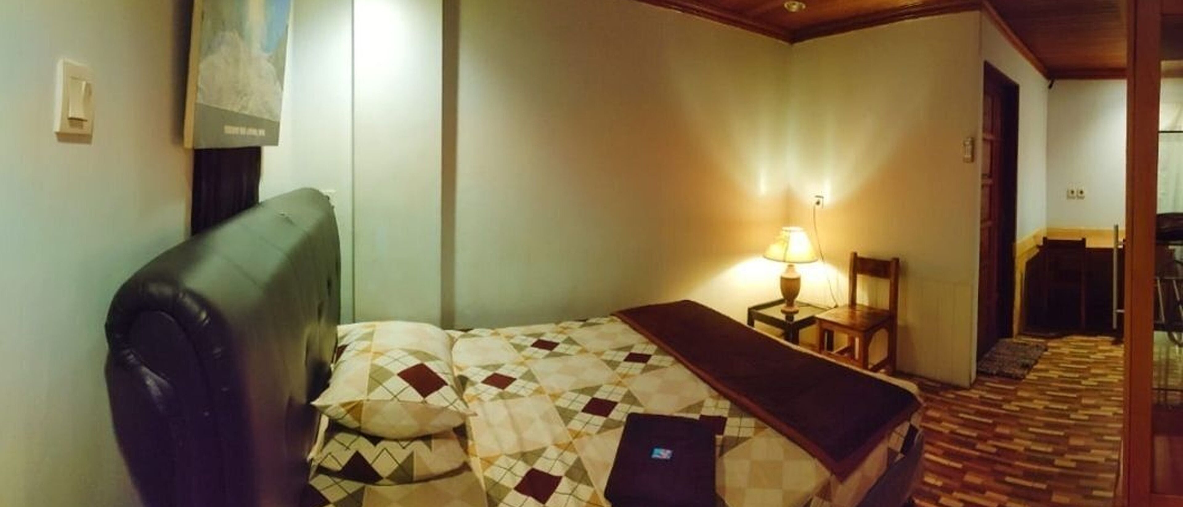 A hotel room with a bed, a chair, a lamp, and a wooden floor.
