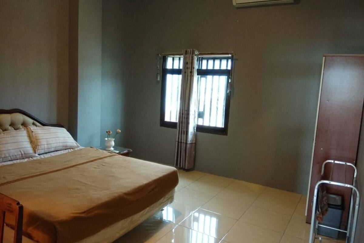 Un dormitorio con cama, ventana con cortinas, mesita de noche y armario.