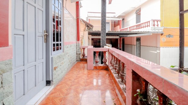 Un pasillo con piso de baldosas, una puerta blanca y un balcón con barandilla roja.