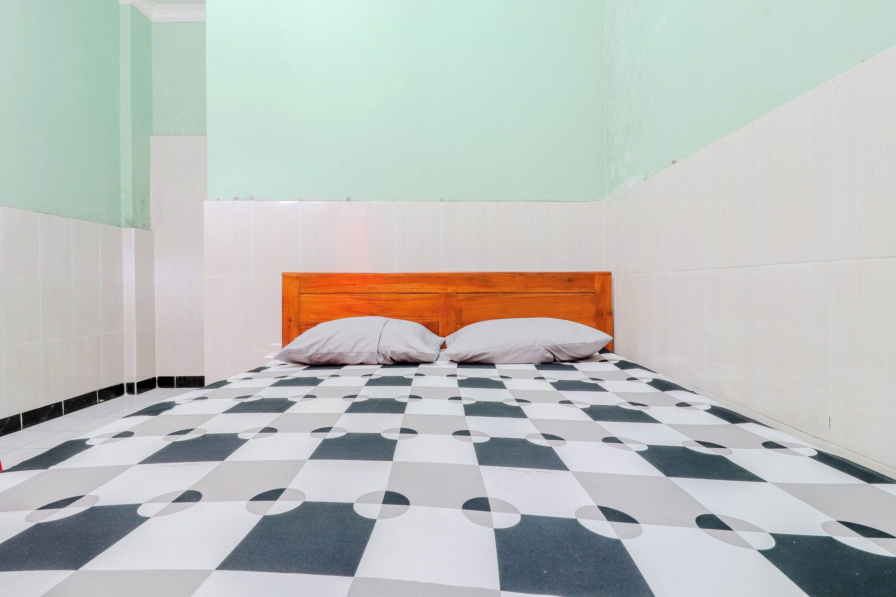 A room with a checkered floor, a wooden headboard, and two pillows.