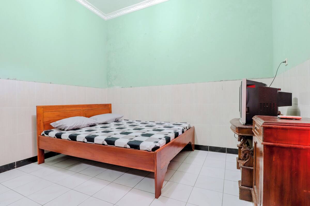 A room with a wooden bed, a small wooden dresser, and a television on a stand.