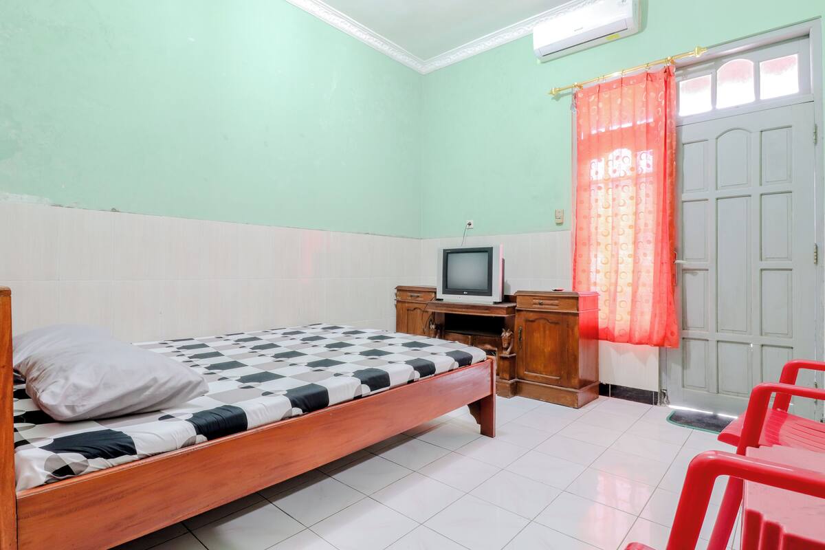 A room with a bed, a television, a wooden cabinet, and a red chair.