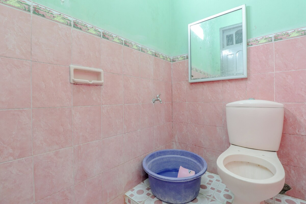 A bathroom with pink tiles, a toilet, a blue plastic basin, and a mirror.