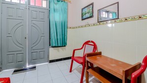 Una habitación con una mesa de madera y dos sillas rojas, una puerta gris, una cortina color turquesa y un espejo en la pared.