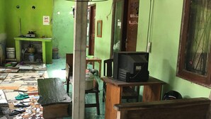 A room with a tiled floor, a television on a wooden stand, and a green wall with a window. - Pak Pur Homestay (Kasihan)