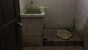 A small, dimly lit bathroom with a toilet, a basin, and a mop leaning against the wall. - Pak Pur Homestay (Kasihan)