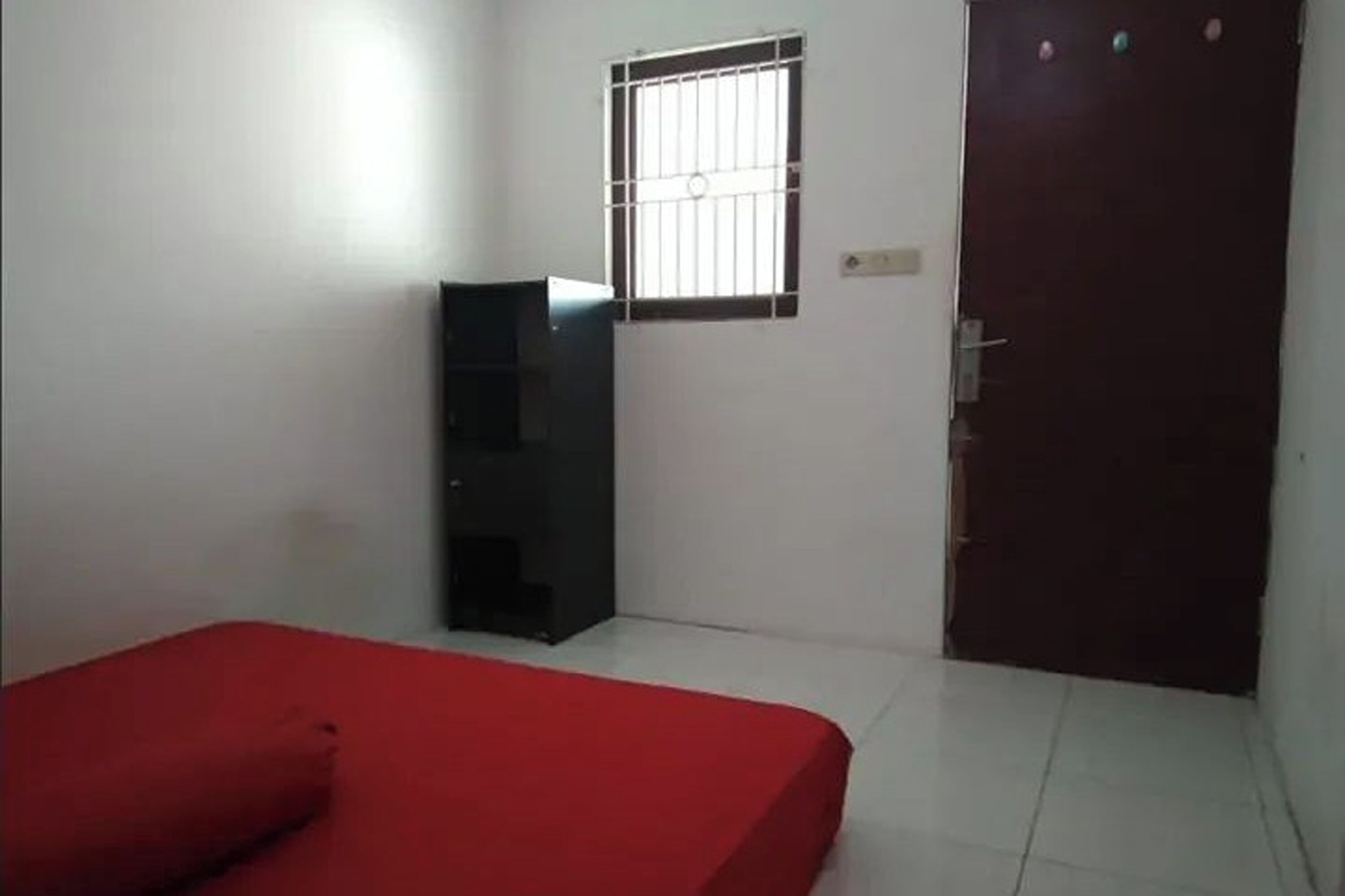 A room with a red bed, a black wardrobe, a barred window, and a closed door.
